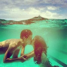 two people in the water with their backs to each other, and one is kissing