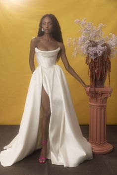 a woman in a white dress standing next to a vase with flowers on the floor