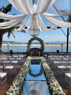 an outdoor wedding setup with white draping and flowers on the aisle, overlooking the ocean