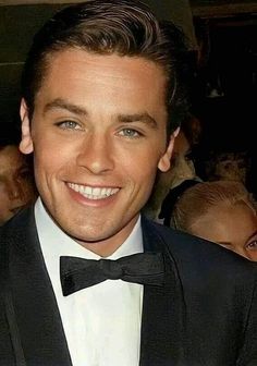 a close up of a person wearing a suit and bow tie smiling at the camera