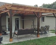 a covered patio with chairs and tables in front of a house that has a wooden pergolan attached to it