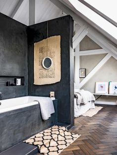 a bathroom with black walls and wood flooring, white bathtub and rugs