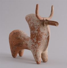 an old clay sculpture of a deer with horns on it's back legs, standing in front of a gray background