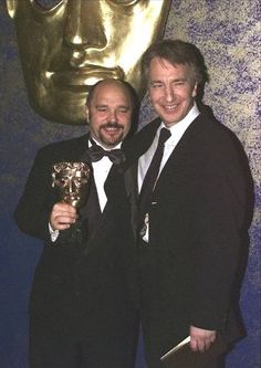 two men standing next to each other in front of a golden statue holding an award