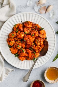 a white plate topped with cooked shrimp next to garlic and seasoning on a table