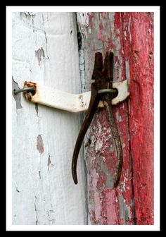 an old rusted metal hook on the side of a red and white painted door