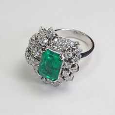 This Platinum Vintage Ring has a stunning large emerald as its center piece. The emerald has strong intense green color and shimmers as you move the piece around! The emerald is set with prongs and on all sides surrounded with sparkly high quality eye clean diamonds in flower petal shapes. There are a total of 57 round brilliants for a total of 2 carats. The ring is a size 7.5.This ring is a great collector's piece with its sparkly flowery design and good quality large emerald!Ring Size: 7.5Tota Green Diamond Platinum Ring Fine Jewelry, Exquisite Green Emerald Platinum Ring, Fine Jewelry Green Diamond Platinum Ring, Dazzling Emerald-cut Emerald Ring, Fine Jewelry Green Diamond Ring In Platinum, Green Platinum Diamond Ring, Dazzling Green Emerald Cut Emerald Ring, Luxury Green Diamond Ring In Platinum, Formal Green Platinum Diamond Ring