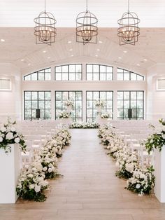 the aisle is decorated with white flowers and greenery for an elegant wedding ceremony in front of large windows