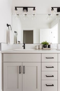 a bathroom vanity with two sinks and three lights on the wall above it is also a large mirror