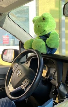 a green teddy bear sitting on the dashboard of a car