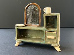 an old green dresser with a mirror and cup on it's top, sitting on a table