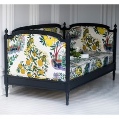 a black bed frame with lemons and flowers on the sheets, in front of a white wall