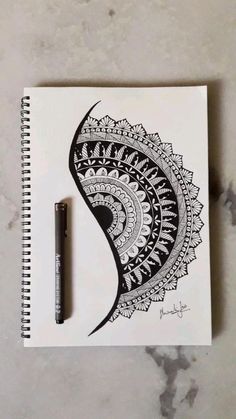 a pen is sitting on top of a spiral notebook with an intricate black and white design