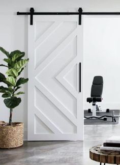 an open white barn door in the middle of a room with a chair and potted plant