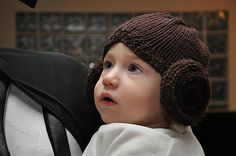 a small child wearing a knitted hat and sitting next to a black chair in a room