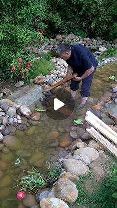 a man is standing in the middle of a stream holding a shovel and digging into some rocks