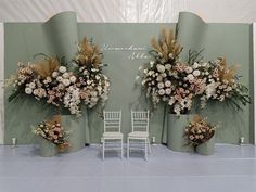 two white chairs sitting next to each other in front of a wall with flowers on it