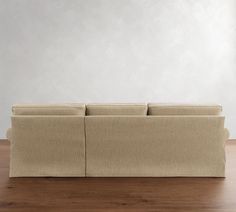 a beige couch sitting on top of a wooden floor next to a white wall in an empty room