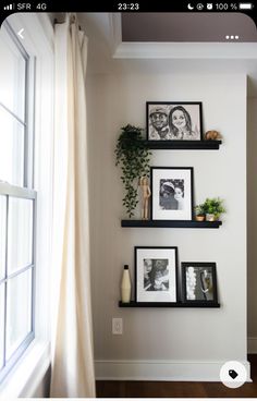 three black shelves with pictures and plants on them in front of a window, next to a white curtain