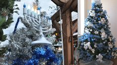 two blue and silver christmas trees in front of a building with lit candles on them