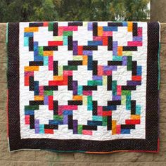 a multicolored quilt hanging on the side of a building with trees in the background