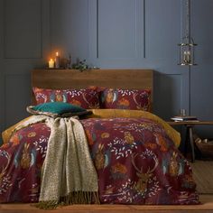 a bed with a red and yellow comforter on top of it next to a wooden headboard