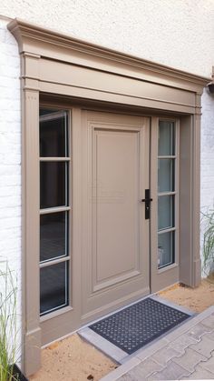 the front entrance to a house with two doors and a door mat on the sidewalk