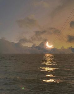 the sun is setting over the ocean with power lines in the foreground and clouds in the background