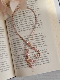 an open book with a necklace on top of it next to a flower and a rose