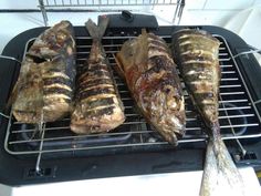 three fish are cooking on the grill and one is being grilled with tongs