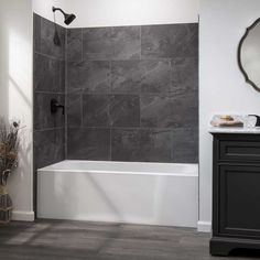 a bathroom with gray tile walls and flooring, including a white bathtub next to a sink