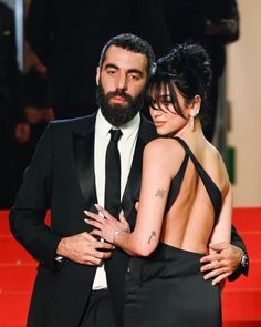 a man and woman standing next to each other on a red carpet with their arms around each other