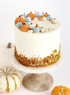 a white cake with orange and blue frosting on a plate next to small pumpkins