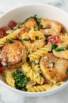 shrimp and scallop pasta with spinach in a white bowl on a marble surface