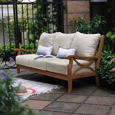 a wooden couch sitting on top of a patio next to flowers and plants in front of a gate