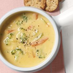 a bowl of broccoli soup next to some crackers on a pink table cloth