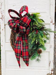 a christmas wreath hanging on the side of a white door with red and green plaid bow