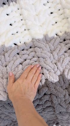 a woman's hand is on top of a gray and white knitted blanket