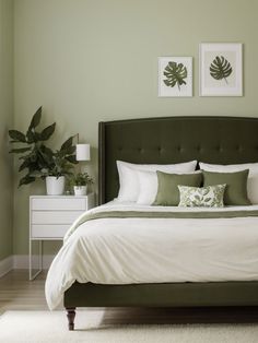 a bedroom with green walls, white bedding and two framed pictures on the wall