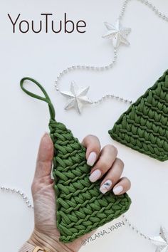 a woman's hand is holding a green crocheted christmas tree ornament