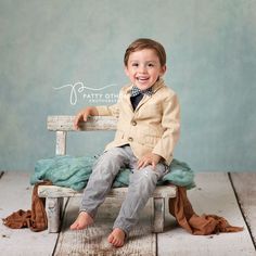 a young boy sitting on top of a wooden bench in front of a blue wall