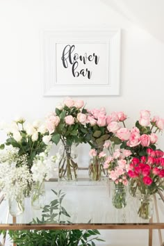 pink and white flowers are sitting in vases on a table with a sign above it