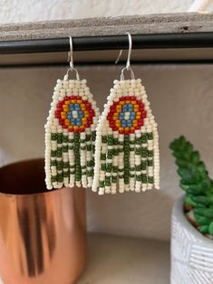 the beaded earrings are on display next to a potted plant