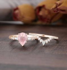 two gold rings with pink stone and white stones on them sitting on a wooden table