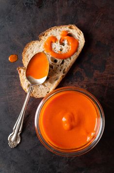 two spoons sit next to a bowl of tomato sauce on a piece of bread