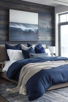 a bed with blue sheets and pillows in a bedroom next to a large window that has wooden planks on the wall