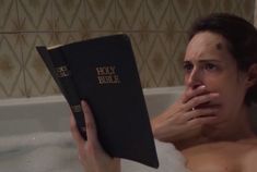 a woman laying in a bathtub holding a bible