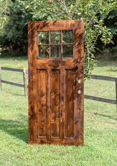 a wooden door sitting in the grass next to a fence and trees with green leaves on it