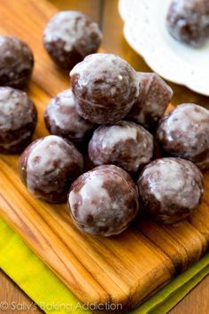 chocolate covered donuts sitting on top of a wooden cutting board next to a white plate