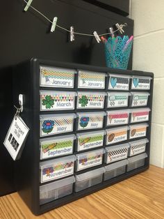 a black cabinet with lots of drawers and labels on the front, hanging from clothes pins